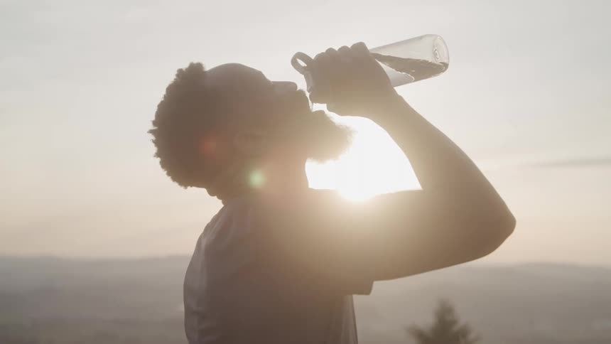 A man tilts his head back and drinks from his water bottle