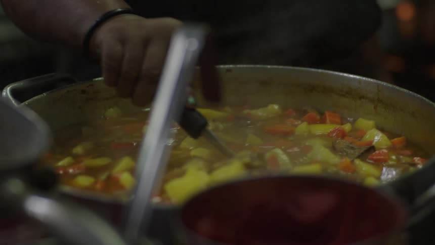 The cook is mixing a pot in the kitchen