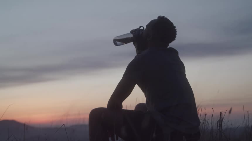 A man sits outside and drinks water