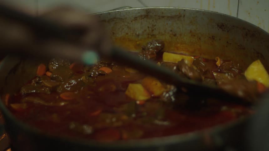 Ladle stirring food being cooked in a pan in sauce