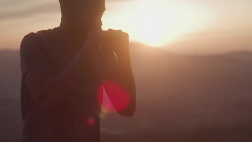 A man throws a punch in silhouette against a dramatic mountain sunset backdrop