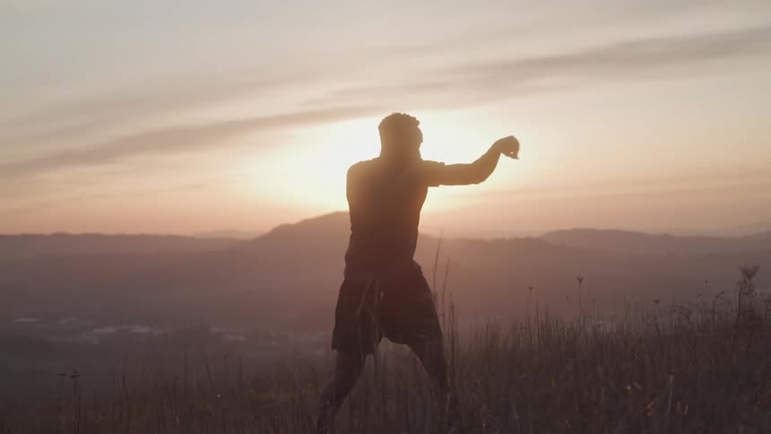 A man shadowboxing on a grassy hill at sunrise or sunset