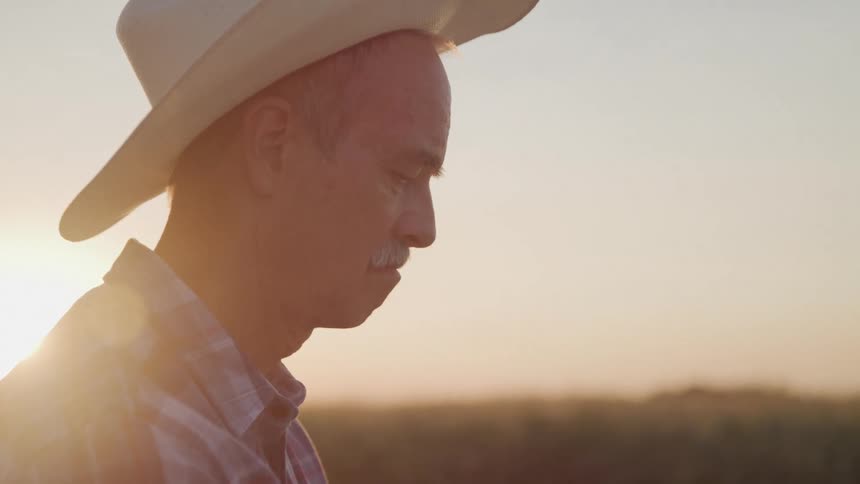 Man stands outdoors in the rural countryside while the sun shines from the red horizon
