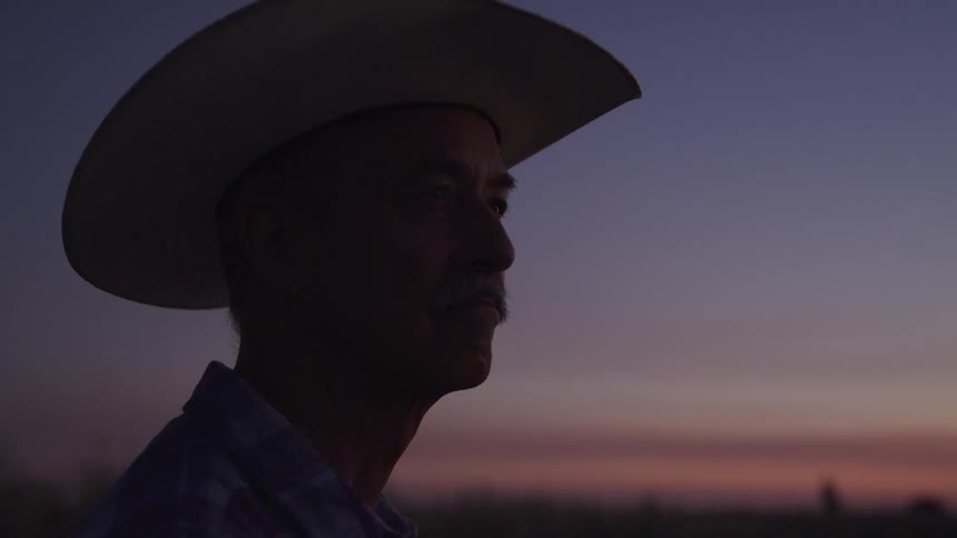 Older man stands outdoors in the rural countryside while red tints the sky