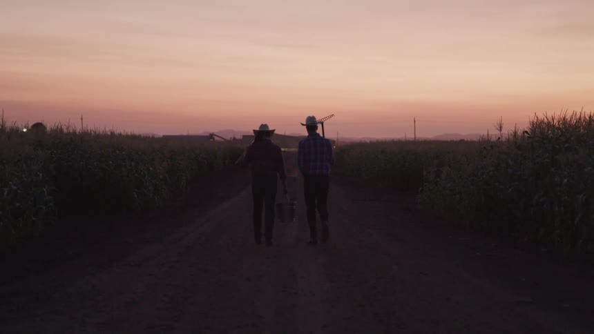 Two farmers carry tools as they walk