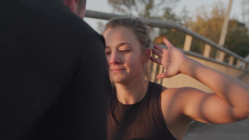 A young woman doing situps on the side of a bridge at midday smiling as a man holds her feet steady on the ground