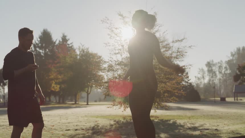 A male trainer motivates a young woman skipping outdoors during the day by clapping