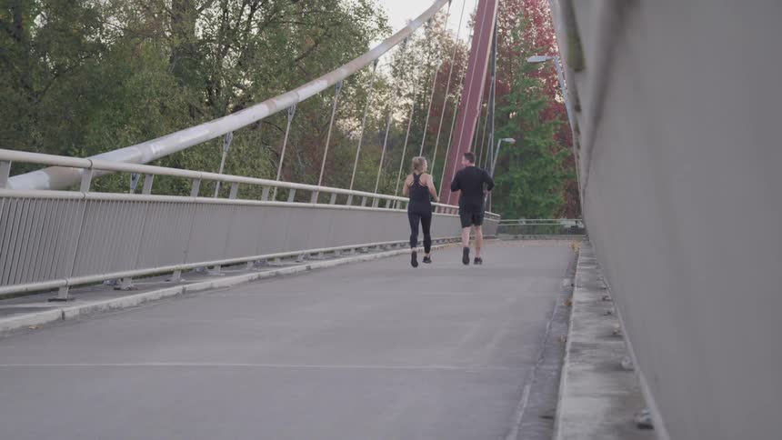 Young man and woman running along a bridge during the day