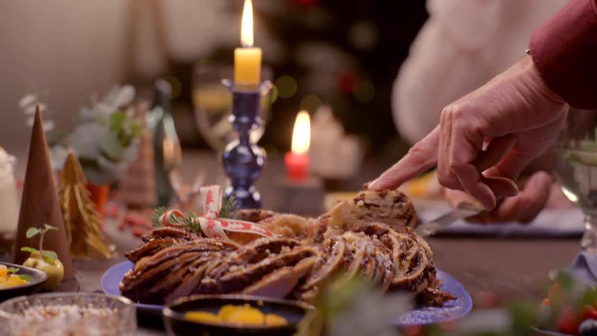 A hand cuts and serves holiday cake at a warm candlelit gathering