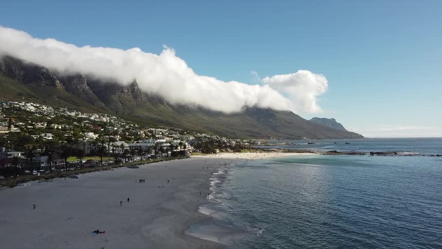 A scenic coastal town lies at the base of cloudcovered mountains along a tranquil beach
