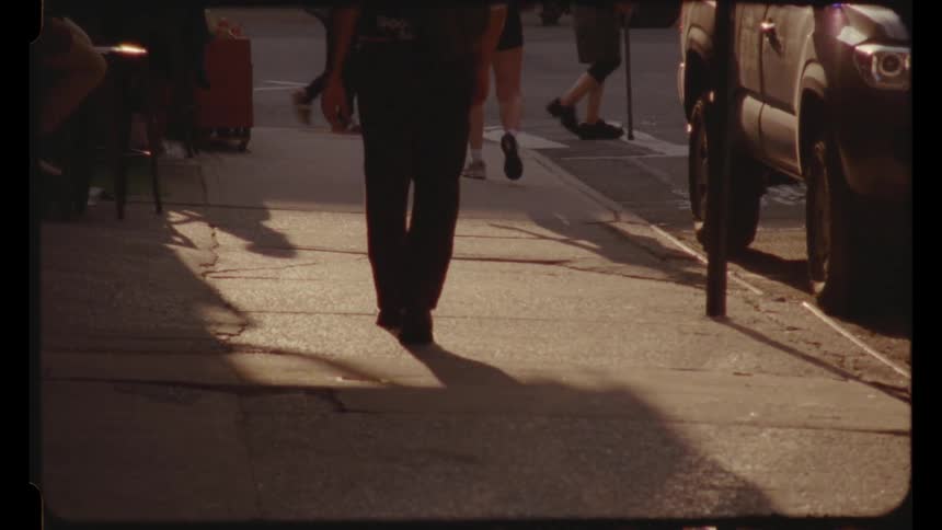 Scattered people shown from the waist down walk on the streets and sidewalk of a city