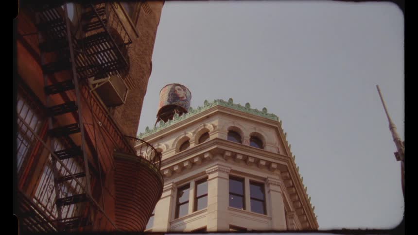 Water tower with a portrait painted on it sits on top of a wedge shaped building in a residential neighborhood