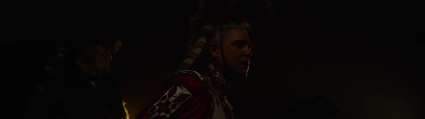 Older native american man dances in a dark area while wearing traditional ceremonial attire