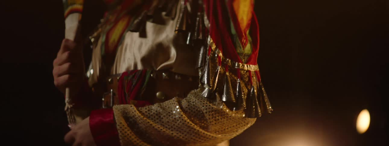 An american indian woman wearing traditional attire stands on a stage proudly showcasing her outfit