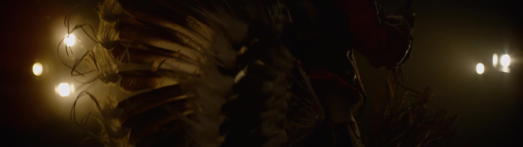 A native american man dressed in traditional feathered attire dances under warm dim lighting