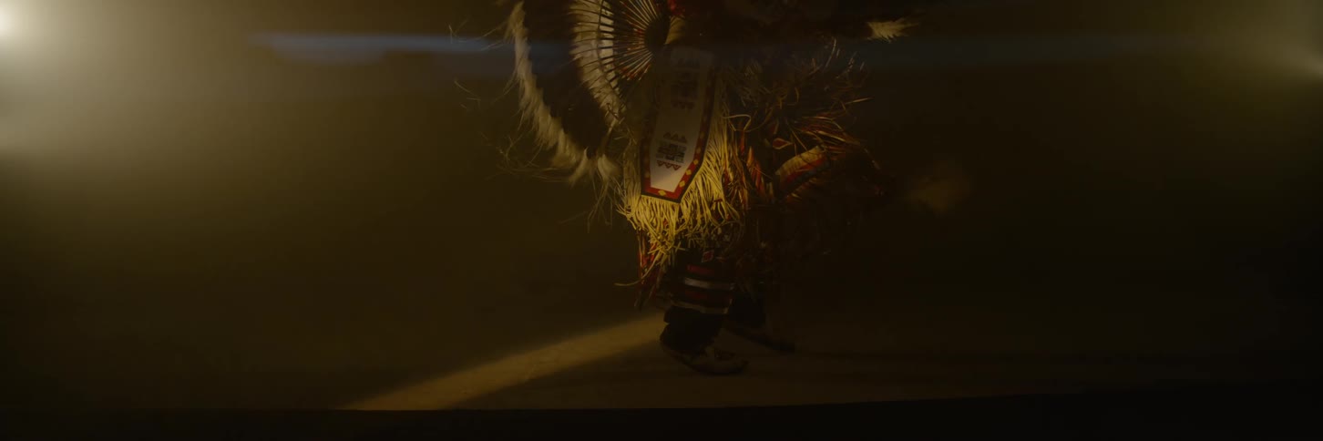A native american man dressed in traditional feathered attire dances under warm dim lighting