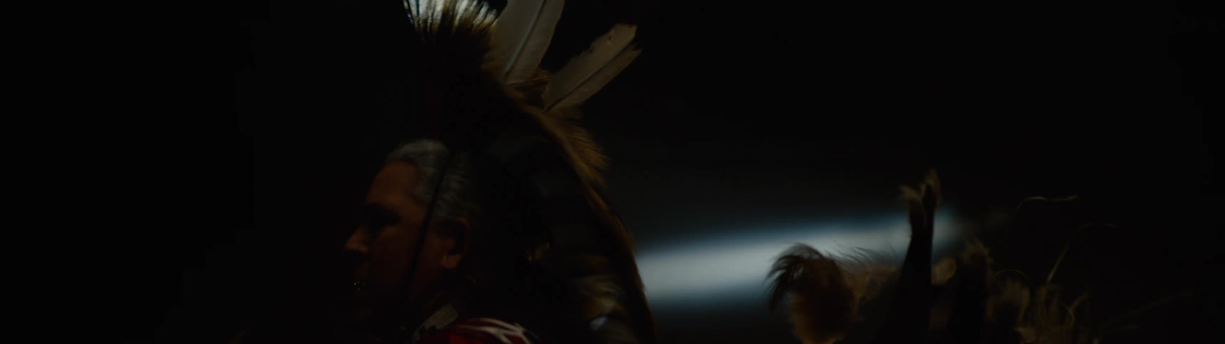 A man in a feathered costume is turning in the dark