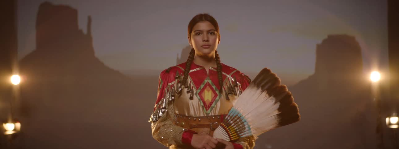 Teenage girl on a stage in traditional indigenous clothing holding a feather fan