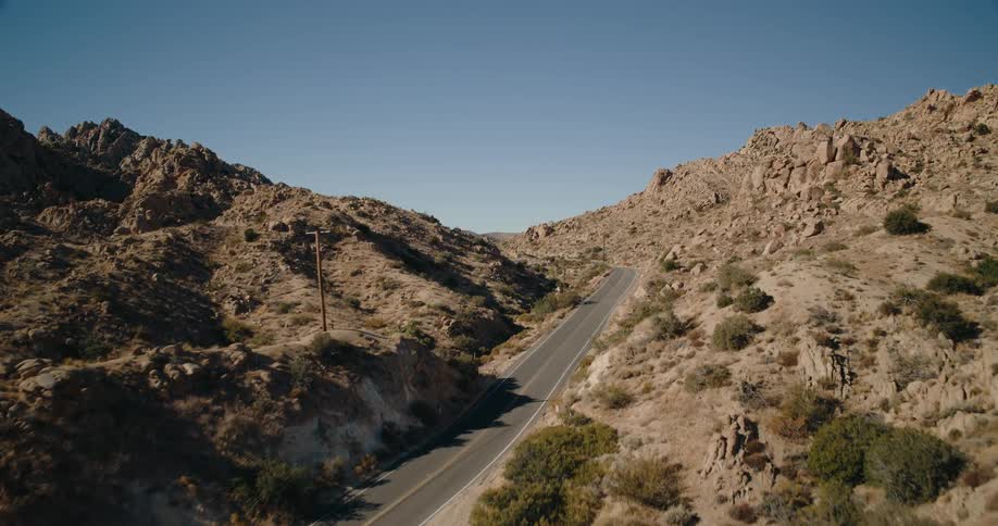 A car drives uphill on a desert highway cutting through rocky rugged terrain