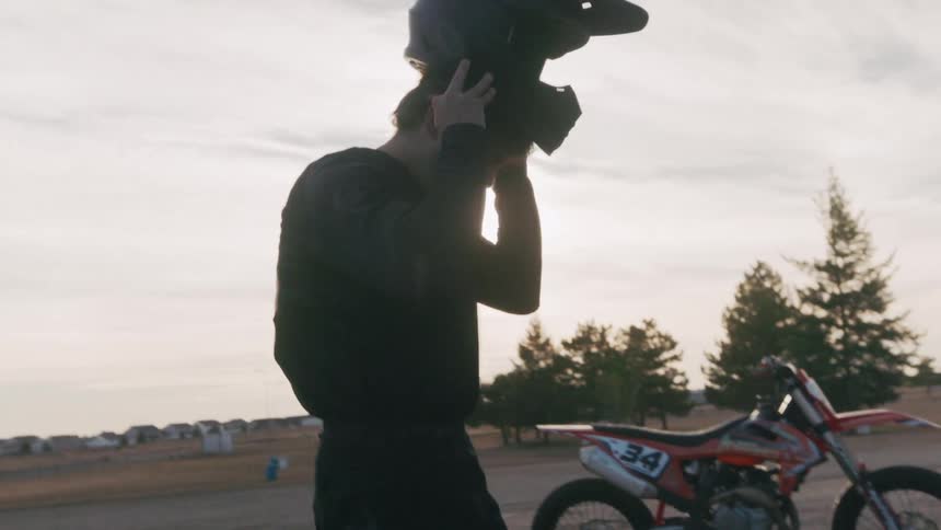 A teenage boy puts on a helmet as he stands next to a dirt bike