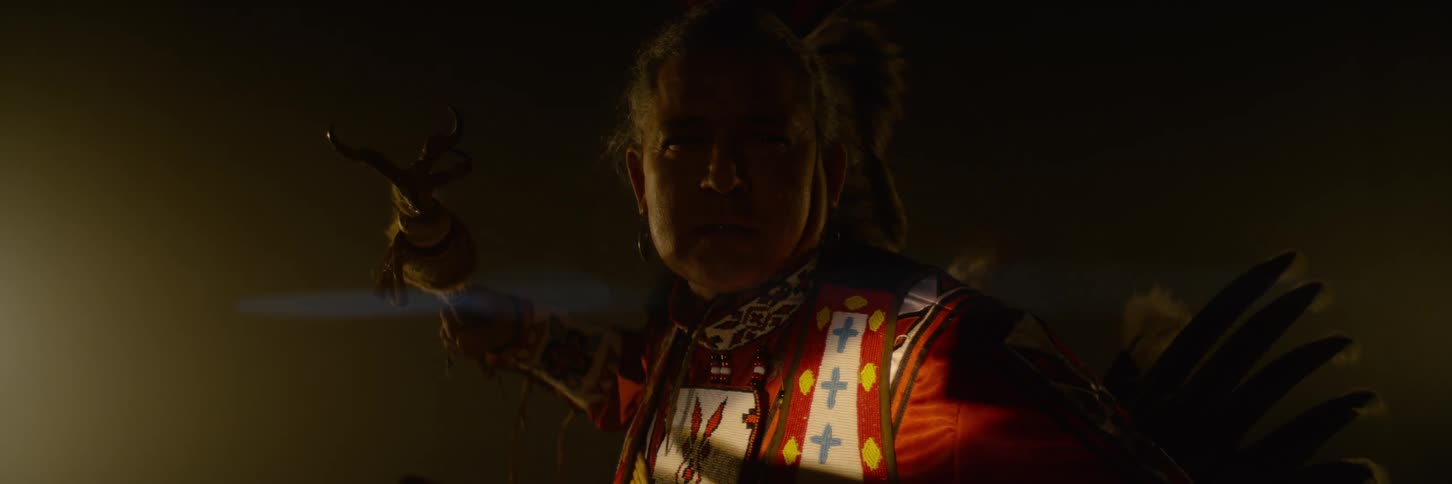An american indian man sits on a stage wearing traditional native attire