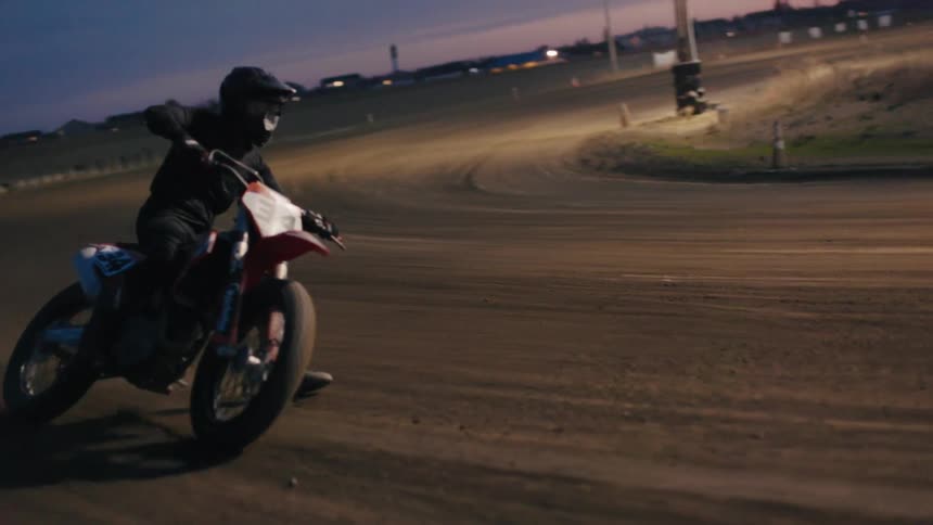 Motocross rider performing a turn on a dirt track at dusk