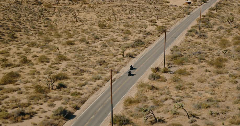 Pair of motorcycles aerial riding along a hwy across the desert