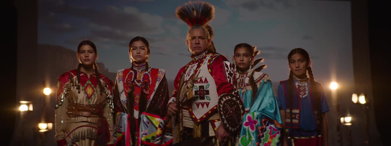 A group of native americans dressed in traditional attire stands on a stage