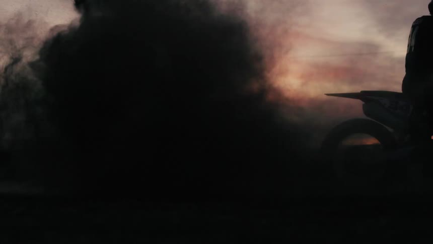 A man on a rally motorcycle accelerating with a lot of smoke coming out of the exhaust pipe