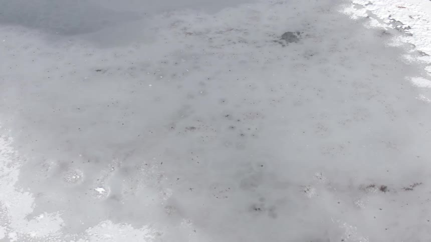 An icy lake with the ice slowly melting gradually revealing the water beneath under the midday sun