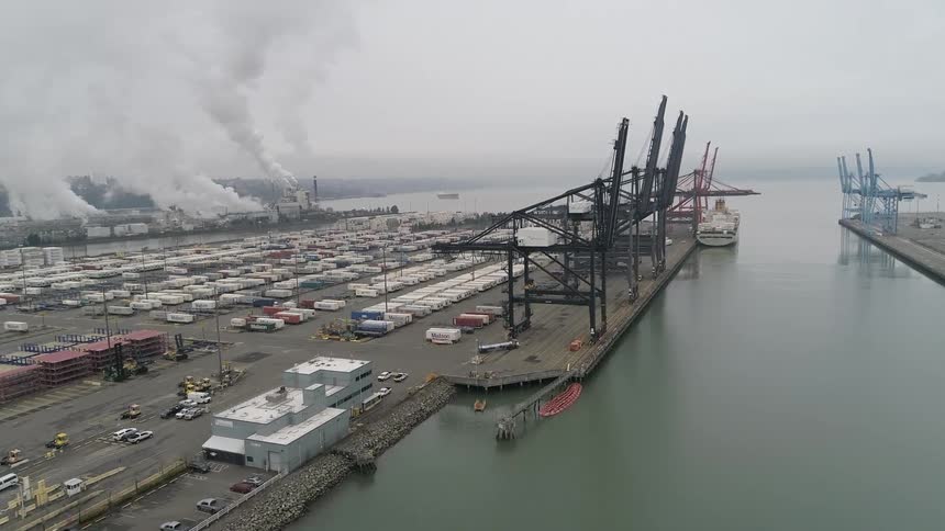 Aerial shot of a seaside port and a factory in the background releasing pollutants