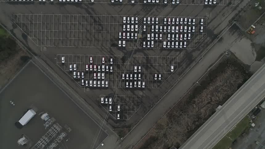 Aerial top view of a triangular shaped parking lot filled with similar white colored vehicles