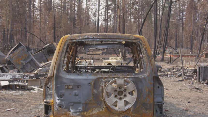 The burnedout husk of an suv sits amidst the charred remains of houses and a forest destroyed by a devastating wildfire