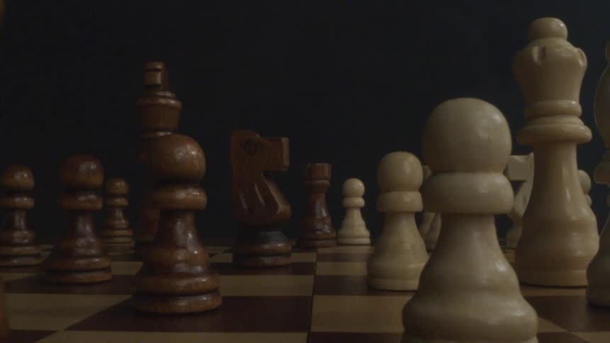 Close up of a chess board with wooden chess pieces all arranged on the dark boxes