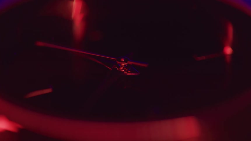 The second hand ticks on a minimalist steel wrist watch under blue and red lighting