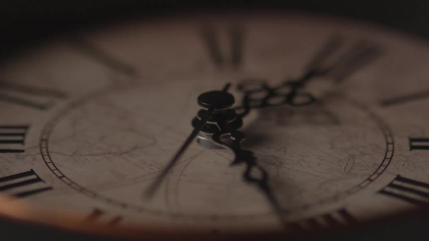 A closeup view of an antique clock face with roman numerals and intricate hands showing a map in the center is dimly lit