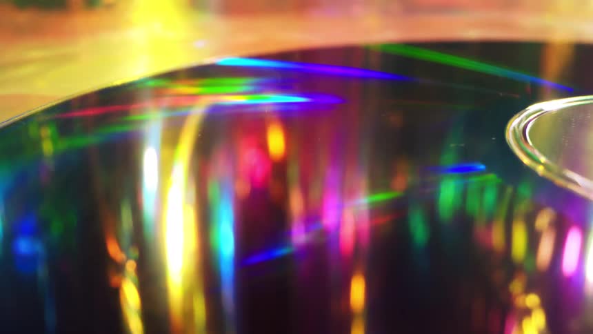 A close up of a compact disc reflecting streams of rainbowcolored light across the surface