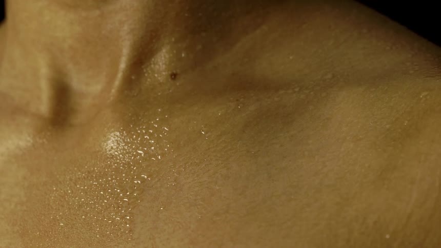 Close up of a persons shoulder covered with water droplets against a dark background