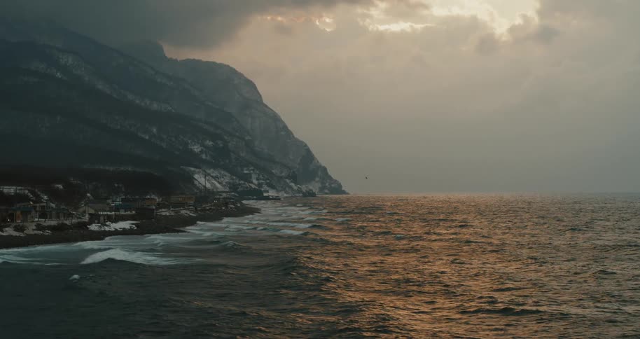 A sea coast a large rocky mountain and a cloudy sky