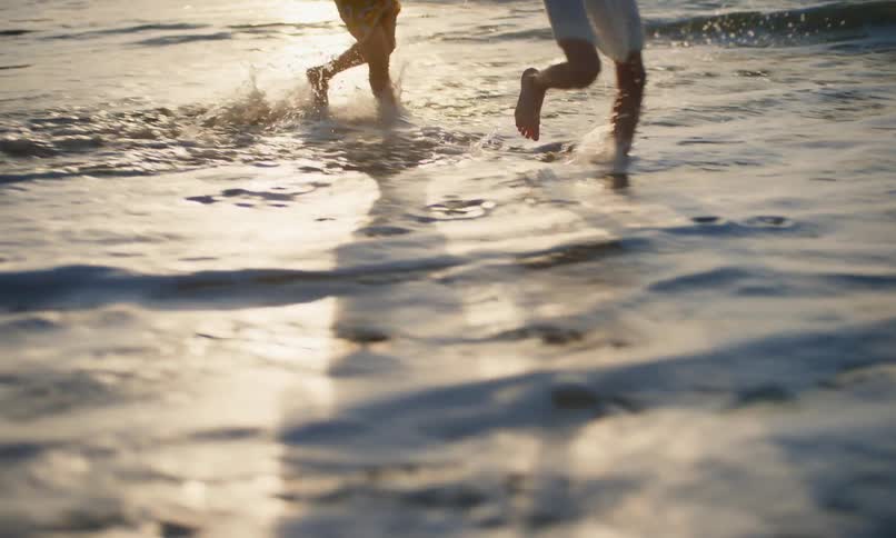Slow motion of two little girls running and chasing each other barefoot in the surf on a beach at sunset.