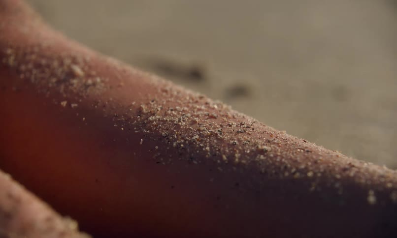 Close up of the texture and varied colors of grains of sand on a person's skin as they lay tanning in the sun at the beach.