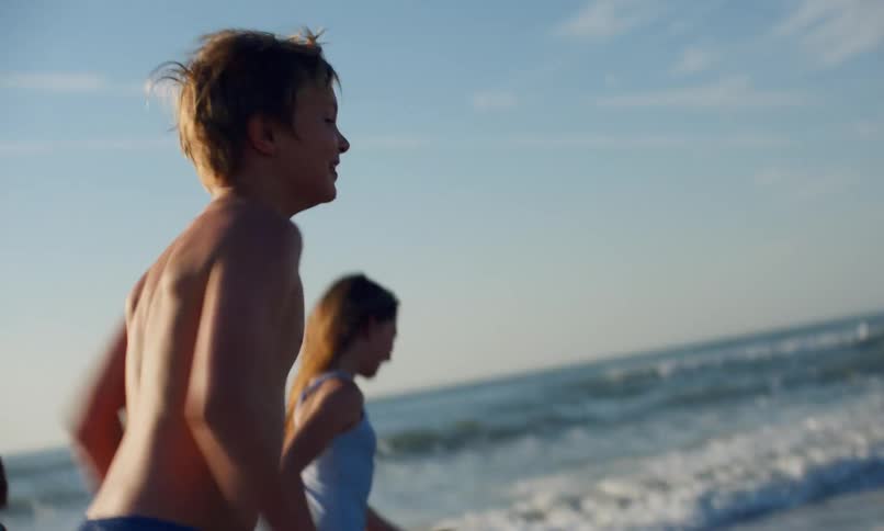 Children race each other running in the wet sand and surf along the shoreline of a beach as waves roll in.