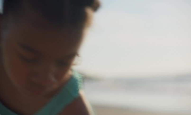 Close up of a little girl of color at the beach digging in the sand with a shovel at sunset.