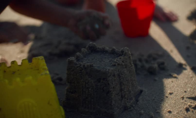 Close up of two children squatting in the sand at the beach using plastic molds to build sandcastles.
