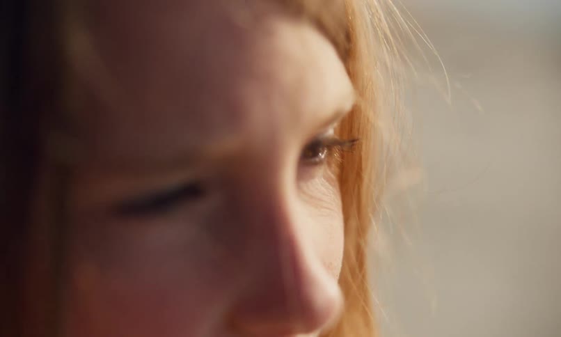 Close up of a young female with red hair standing outdoors in the evening sun as a gentle wind softly blows through her long hair.