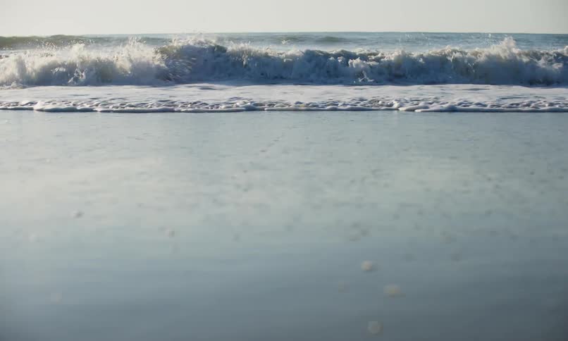Close up view from the sand surface of ocean waves pushing surf directly in to the camera on the shore of a beach at sunset