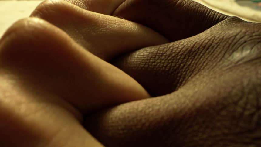 Close up of a black person interlocking their fingers with another person on a table surface
