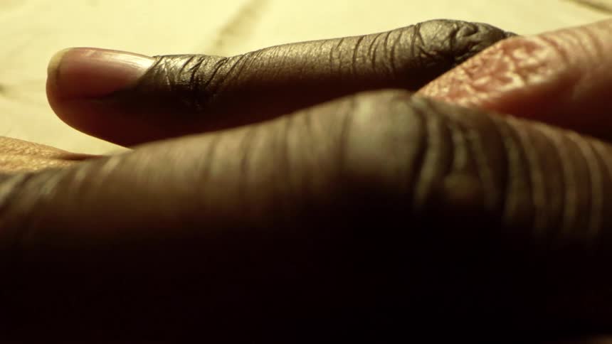 Close up of a black person and a white person interlocking fingers on a table surface