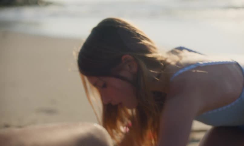 Close up views of three diverse children wearing swimsuits at the beach while playing in the sand with the waves and surf coming in behind them.