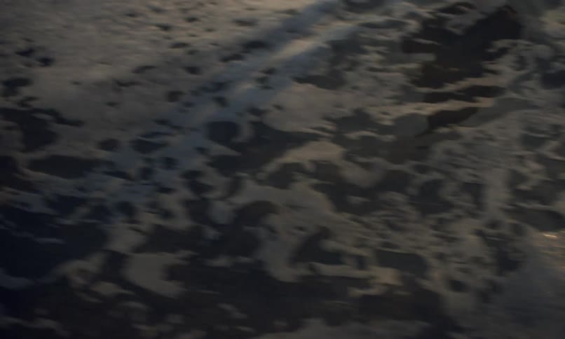 Close up of a person's lower legs and shadow who is standing in the surf at the shoreline of a beach as the tide comes in at sunset